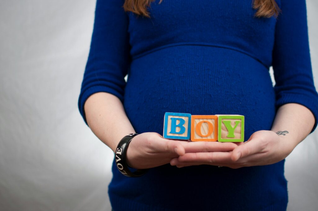 Pregnant woman in blue dress holds 'boy' blocks, symbolizing a baby boy announcement.